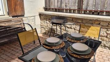 Un espace extérieur aménagé pour les repas, avec un mur en pierre en arrière-plan, un barbecue et une clôture en bois.