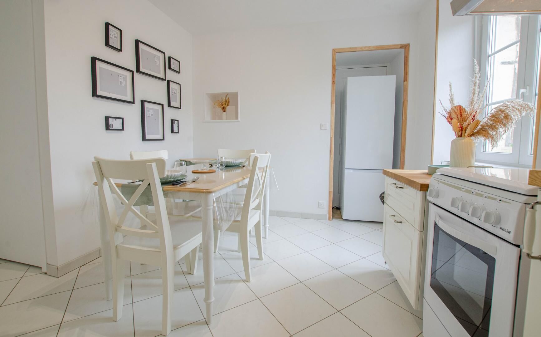 Una cocina moderna con armarios blancos, una mesa de comedor con sillas y un refrigerador.