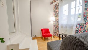 A room with a white bed, a red chair, a floor lamp, and a window with floral curtains.