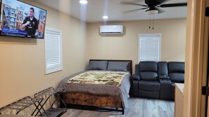 Une chambre à coucher comprenant un lit, un fauteuil en cuir noir, un ventilateur de plafond et un appareil de climatisation.