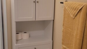 A corner bathroom with a white cabinet, a towel rack with a yellow towel, and a toilet paper holder.