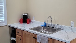 A kitchen with a sink, wooden cabinets, a marble countertop, and a window with blinds.