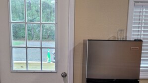 A kitchen with a refrigerator, a door with a window, and a doormat.