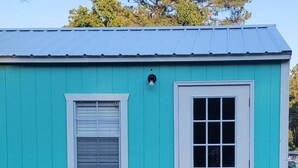 A small, single-story building with a turquoise exterior, a wooden deck, and a white door.