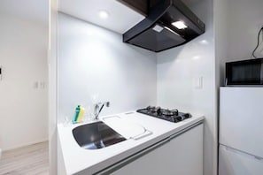 A compact kitchen with a gas stove, a sink, and a microwave. - Renaissance Court Jiyugaoka (Tokyo)