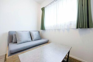 Una habitación con un sofá gris, una mesita y una ventana con cortinas verdes.
