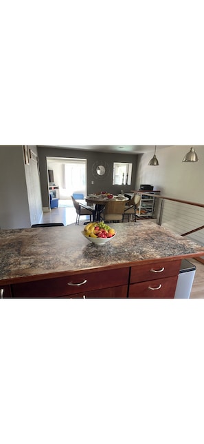 A kitchen with a granite countertop, a fruit bowl, and a dining area with a table and chairs.