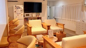 Ein modernes Wohnzimmer mit Flachbildfernseher, Kühlschrank mit Magneten, Korbstühle, einer Couch und einem Esstisch.
