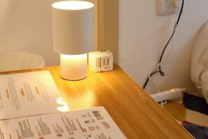 Une table en bois sur laquelle se trouvent une lampe blanche, une multiprise et des documents.