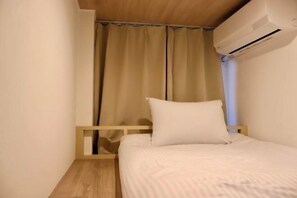 Une chambre à coucher avec un lit, une tête de lit en bois, des rideaux beiges et un appareil de climatisation.