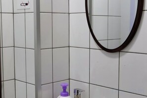 Un baño con paredes de azulejos blancos, un espejo y una botella morada.
