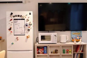 Een keuken met een witte koelkast, een magnetron en een flatscreen televisie die aan de muur is bevestigd.