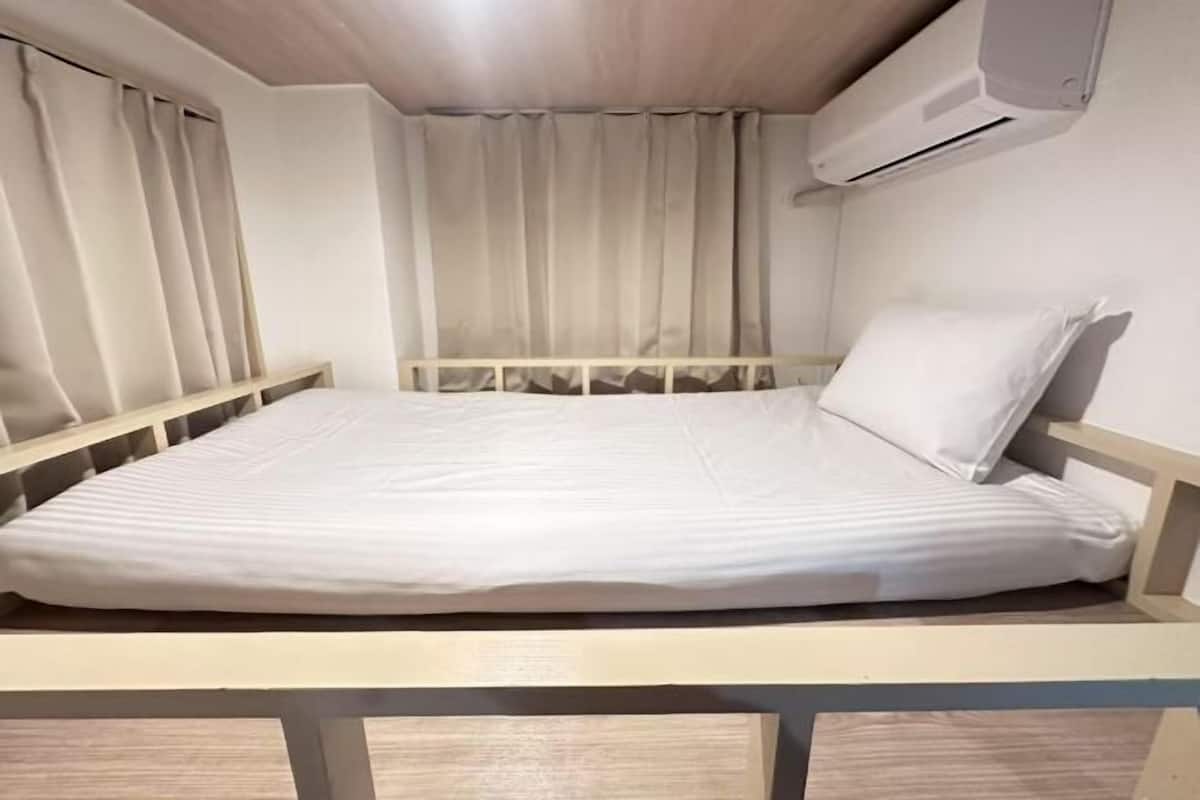 Ein Einzelbett mit Holzrahmen, weißer Bettwäsche und einer Wand-Klimaanlage.