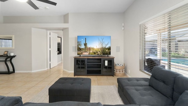 A modern living room with a flat-screen TV, grey sofas, a coffee table, and a ceiling fan.