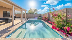 A swimming pool with a pergola and outdoor seating, surrounded by a brick wall and flowering plants.