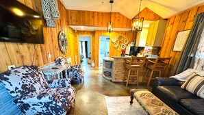 A cozy living room with a sofa, a coffee table, and a dining area with a kitchen in the background. - The Apartment of GRACE! (Corpus Christi)