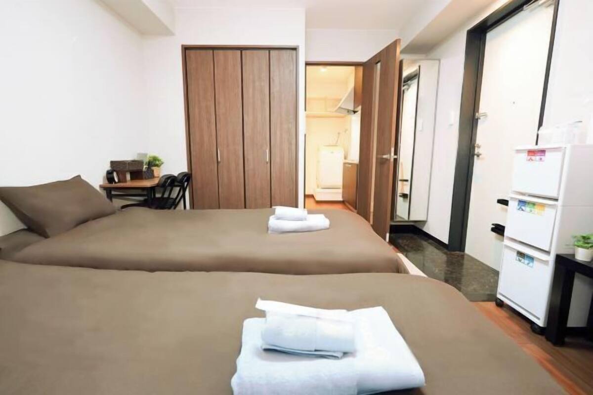 Een hotelkamer met twee bedden, een bureau met stoel, een garderobe en een koelkast.