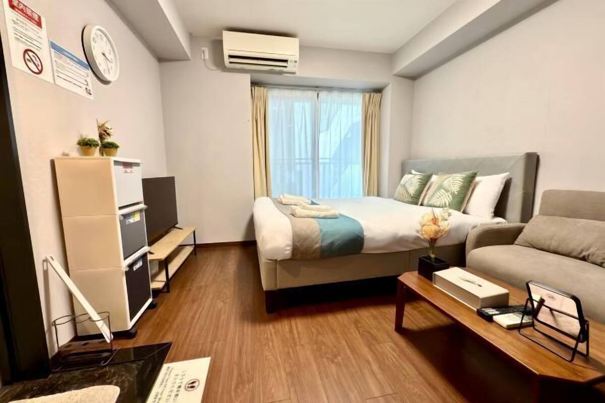 Hotelkamer met een bed, een bank, een bureau, een airconditioner, een klok en een raam met gordijnen.