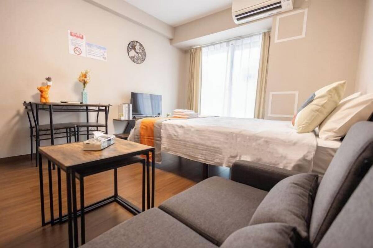 Hotelkamer met een bed, een slaapbank, een bureau met stoel, een televisie en een klein tafeltje met een teddybeer en bloemen.