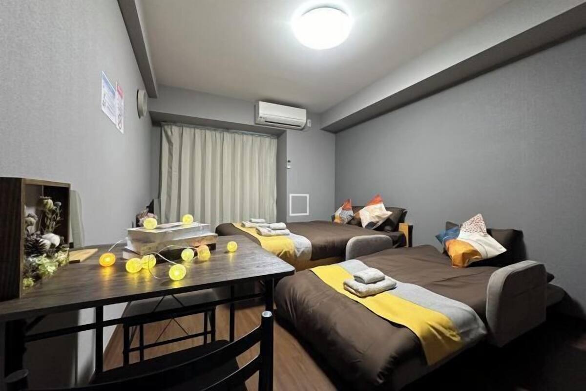 Een hotelkamer met twee enkele bedden, een kleine tafel met lamp, een airconditioning en een raam met gordijnen.