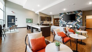 Eine moderne Hotellobby mit einer zentralen Insellounge, Sitzgelegenheiten und einem an der Wand befestigten Flachbildfernseher.