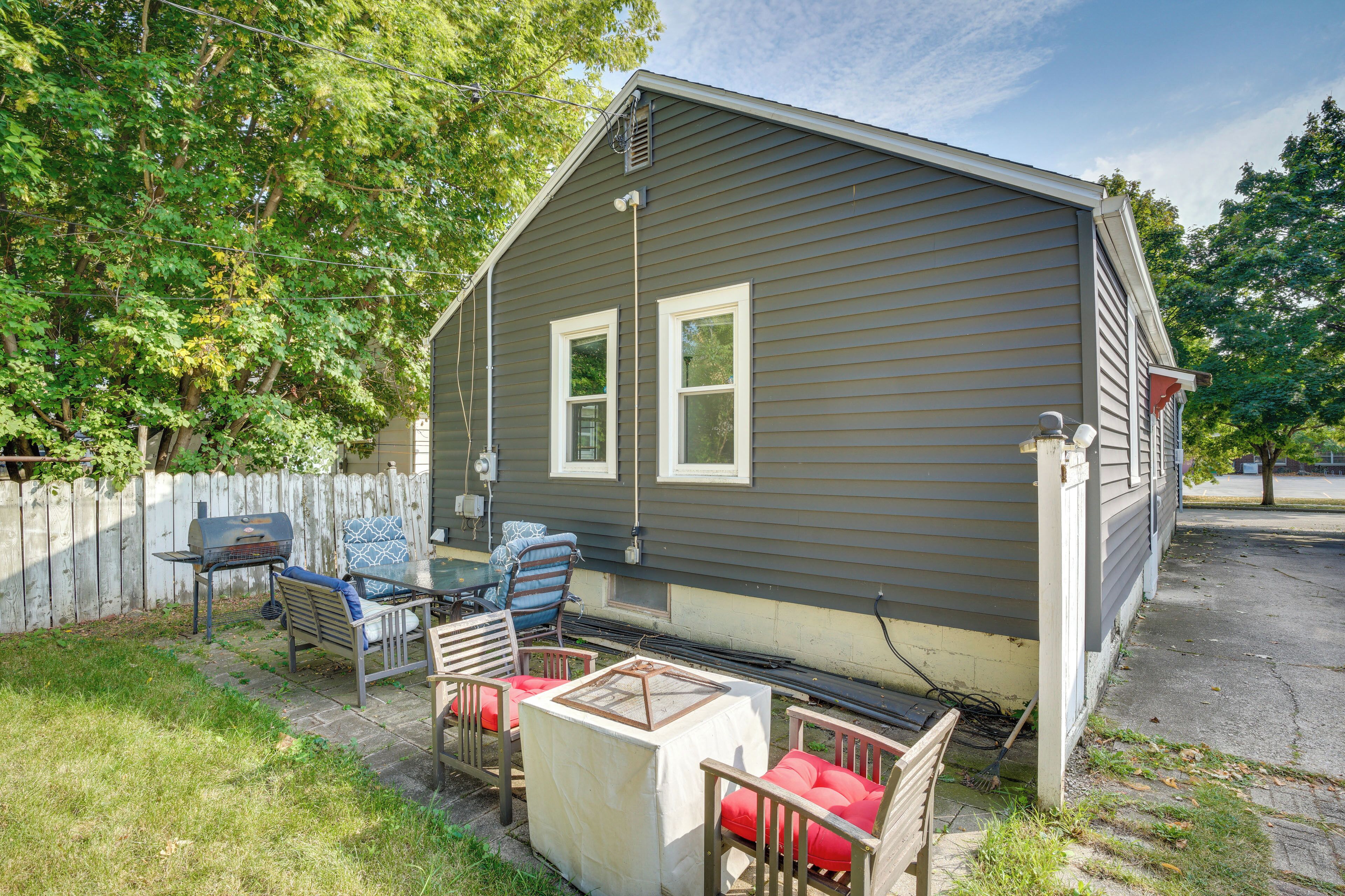 A small, single-story house with a gray exterior, a white front door, and a small porch area with a table and chairs.