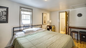 A bedroom with a bed, a window with blinds, a door, a wall clock, and a small table with a lamp. - 2 Mi to Lake Winnebago: Cozy Fond du Lac Studio (Fond du Lac)