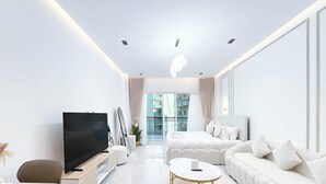 A modern living room with a flat-screen TV, a white sofa, a round coffee table, and a large window offering a view of the city. - Relaxing ST Getaway Balcony, Pool & Gym Access (Dubai)