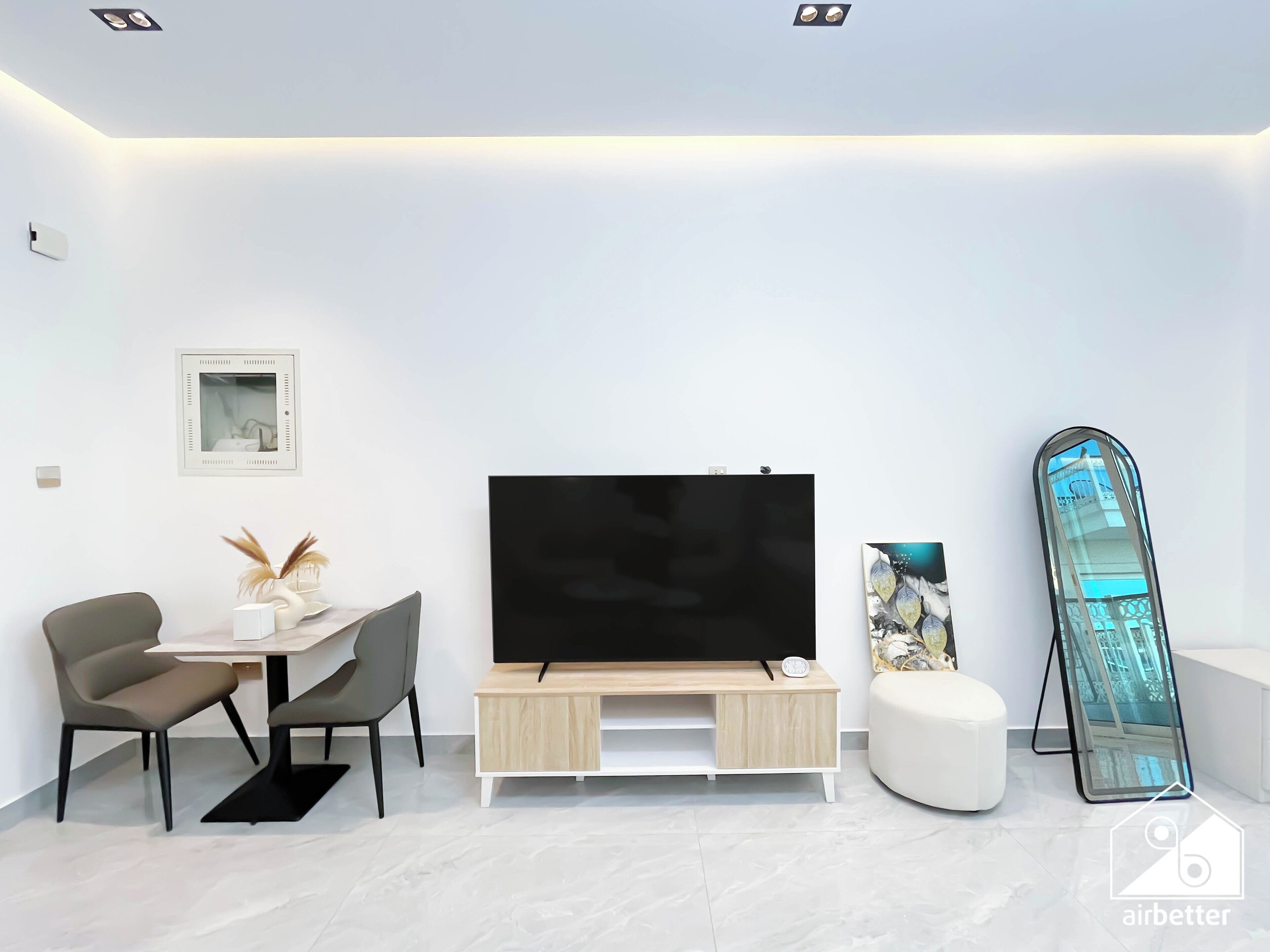 Una sala de estar moderna con una televisión de pantalla plana, una mesa de comedor con sillas, un sofá blanco y una obra de arte grande enmarcada.