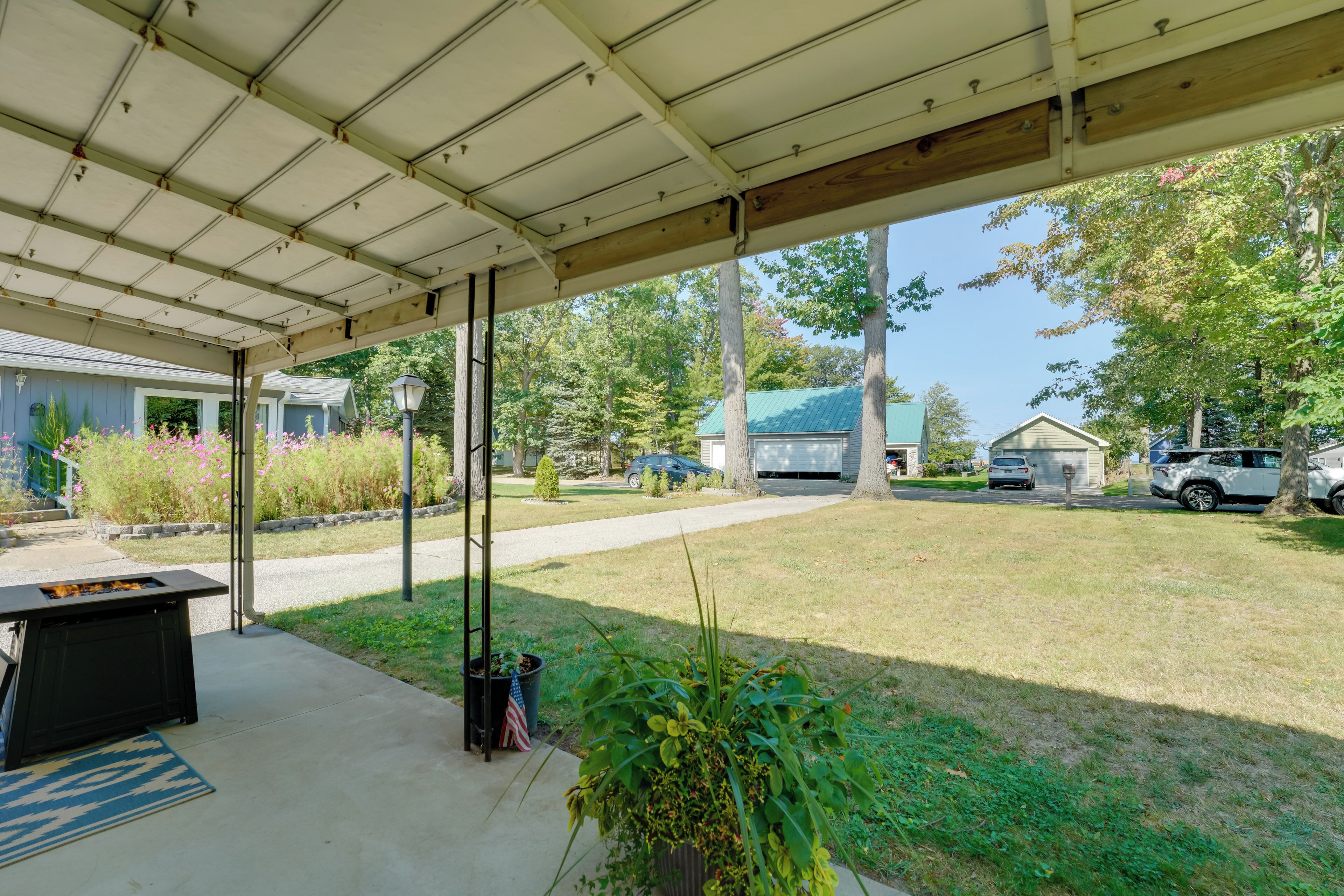 A covered patio area with a barbecue grill, potted plants, and a view of the neighborhood.