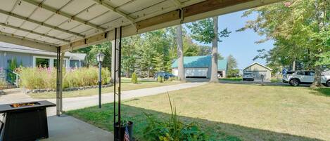 A covered patio area with a barbecue grill, potted plants, and a view of the neighborhood.
