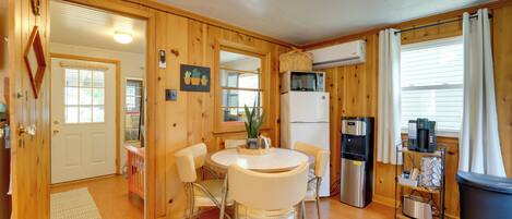 A compact kitchen with wooden walls, a white refrigerator, a microwave, a coffee maker, and a small dining table with chairs.