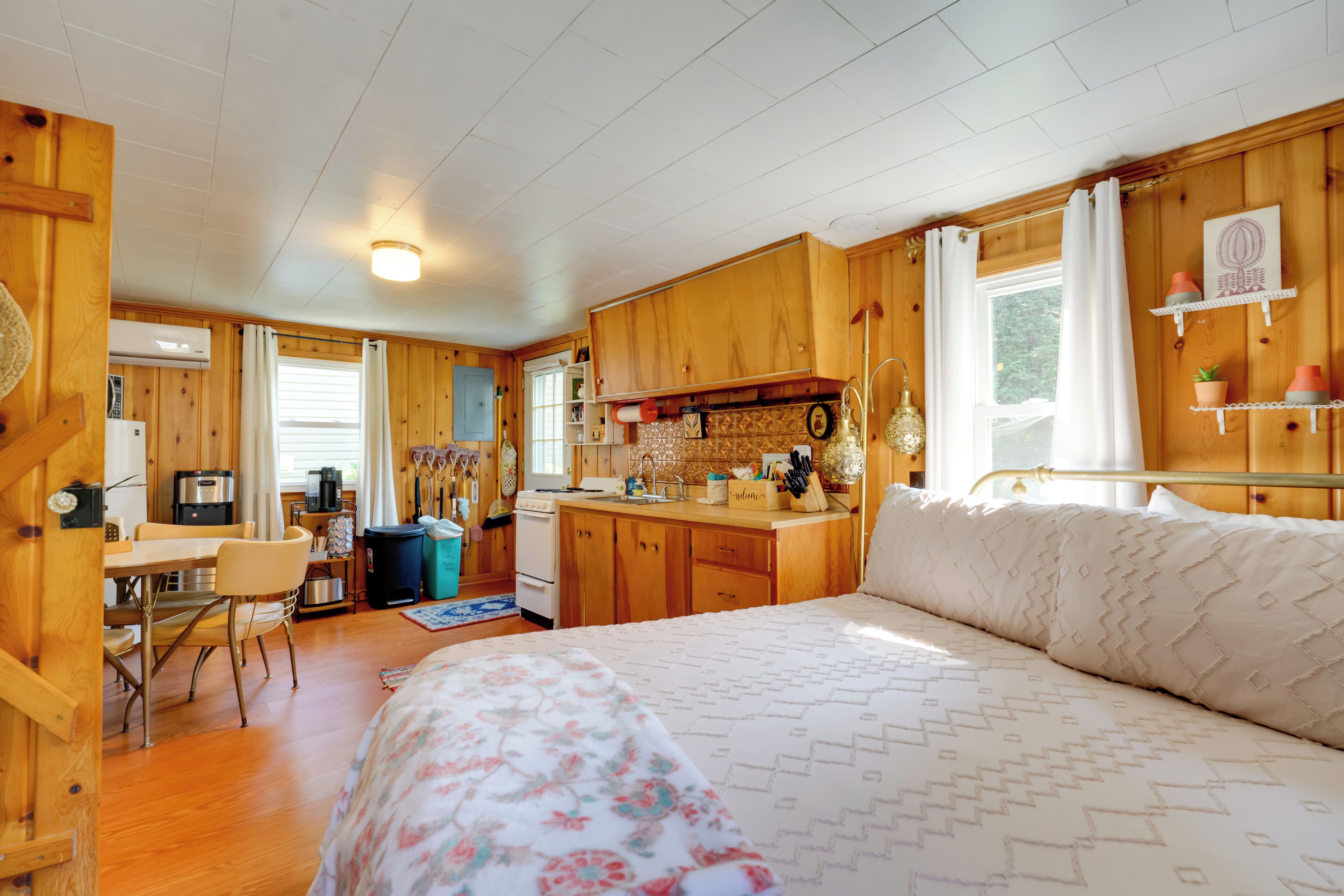 Una habitación acogedora de estilo cabaña con paredes de madera, una cama con ropa de cama estampada, una kitchenette y un comedor.