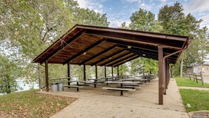A covered picnic area with benches and trash cans, surrounded by trees and a body of water. - Fish, Boat & Hike: Norfork Lake Studio Near Marina (Mountain Home)