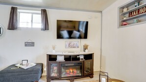 A living room with a fireplace, a television mounted on the wall, a small table with books, and a shelf with decorative items. - Fish, Boat & Hike: Norfork Lake Studio Near Marina (Mountain Home)