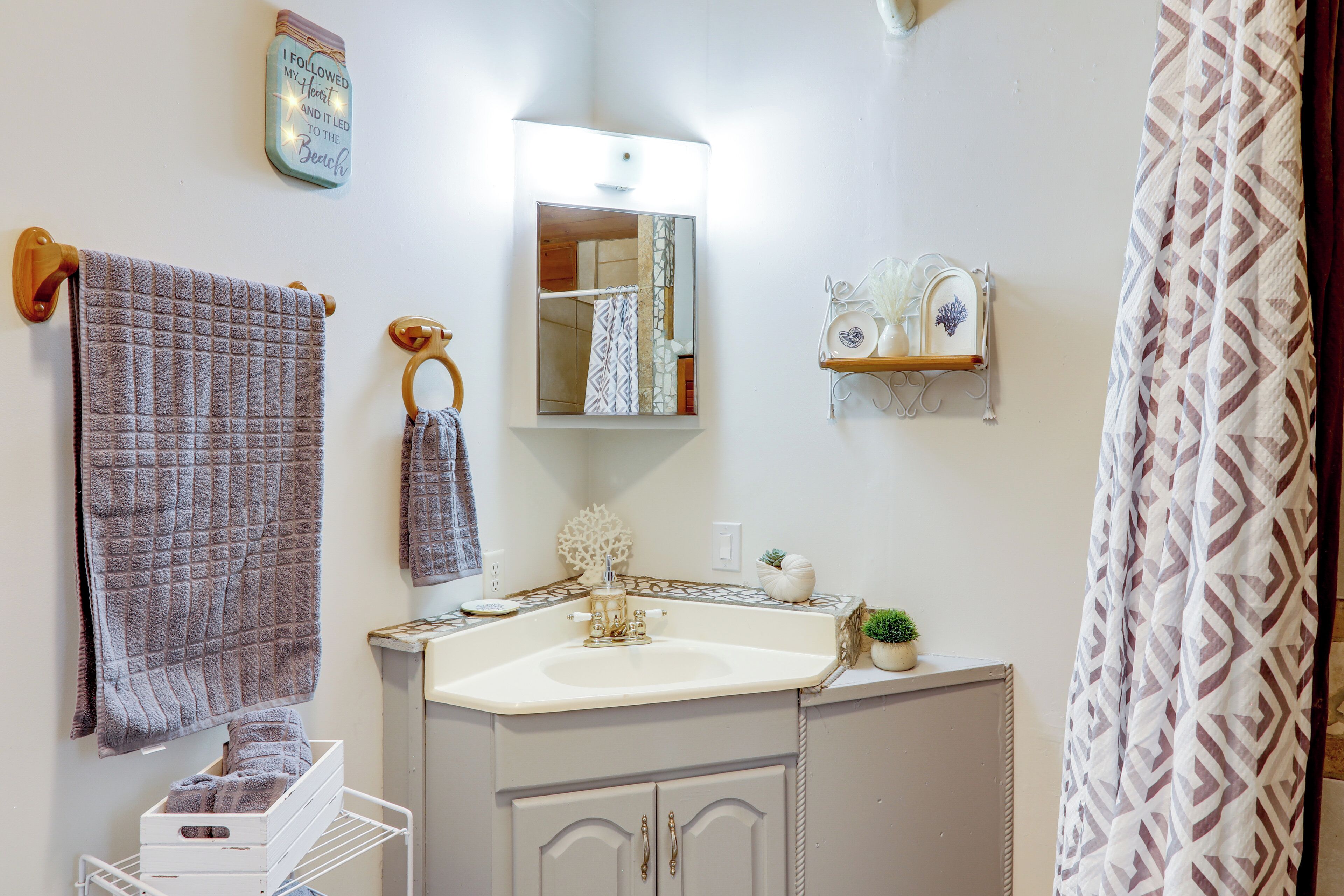 A bathroom with a white sink, a mirror, a towel rack, a shelf with toiletries, and a patterned shower curtain.