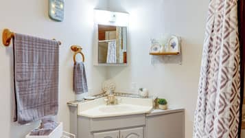 A bathroom with a white sink, a mirror, a towel rack, a shelf with toiletries, and a patterned shower curtain.