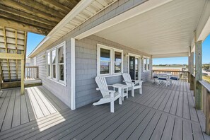 A covered porch with white Adirondack chairs, a wooden deck, and a view of the ocean.