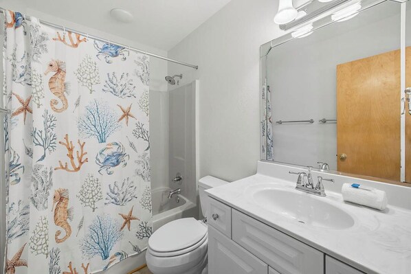 A bathroom with a shower curtain featuring sea life, a bathtub, a toilet, a sink, and a mirror.