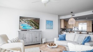 Un salon moderne avec un canapé blanc, une table basse ronde et un meuble gris. Un tableau représentant une scène de plage est accroché au mur.
