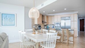 Une cuisine moderne avec des meubles blancs, un grand îlot central et un coin repas doté de chaises blanches.