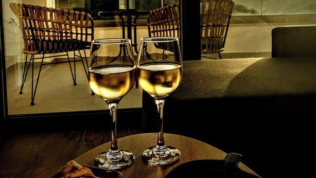 A table with two glasses of white wine, a bowl of fries, and a view of a mountainous landscape through large windows. - LefkoParga luxury Suites  (Parga)