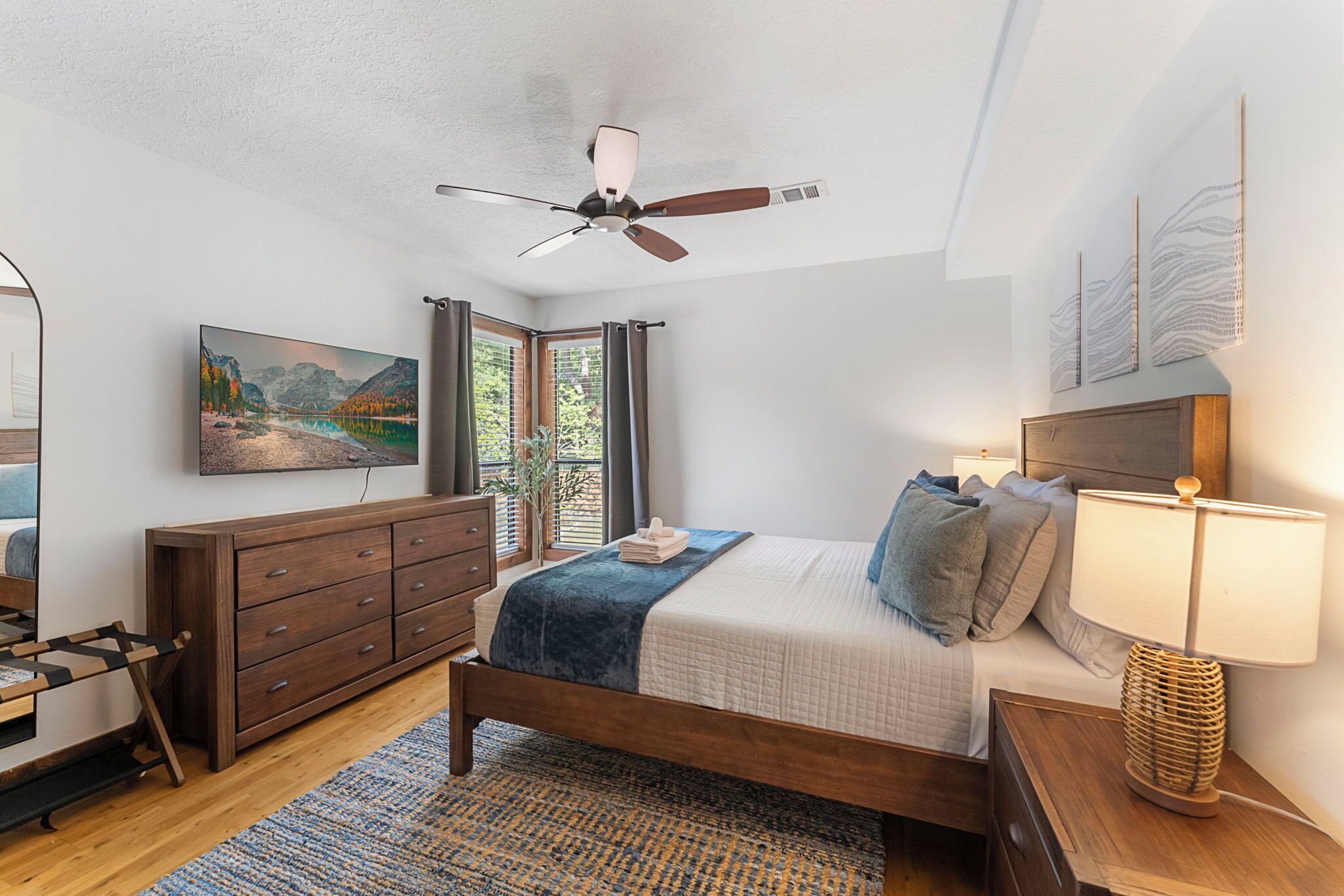 A bedroom with a bed, bedside table, lamp, dresser, and a painting on the wall.