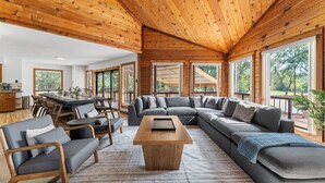 A spacious living area with a wooden ceiling, a large sectional sofa, a coffee table, and a dining area with a table and chairs.