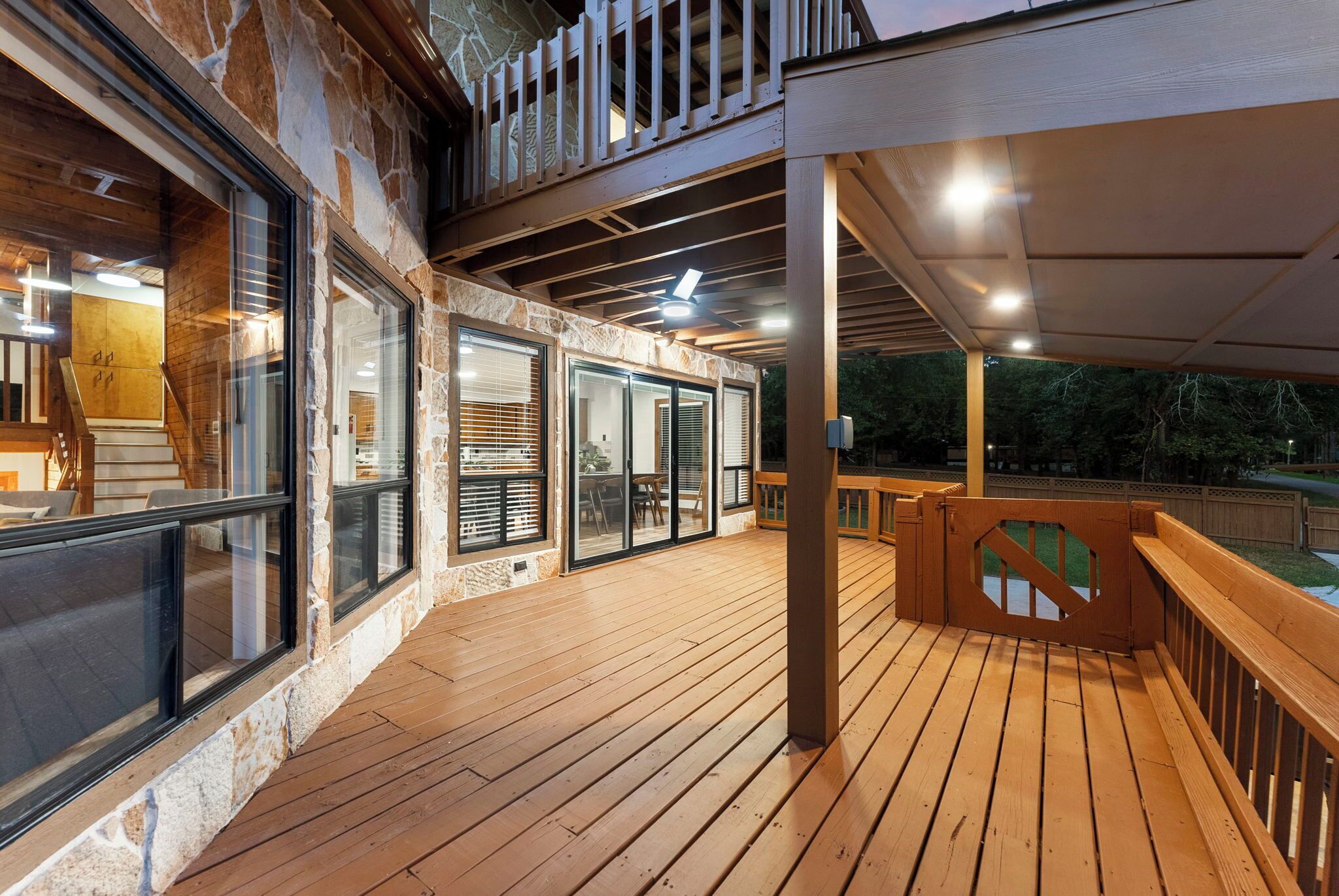 A wooden deck with a stone wall, glass doors, and a wooden railing.