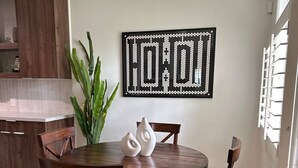 Una zona de menjador amb una taula rodona de fusta, quatre cadires, una planta en test i una peça decorativa a la paret.