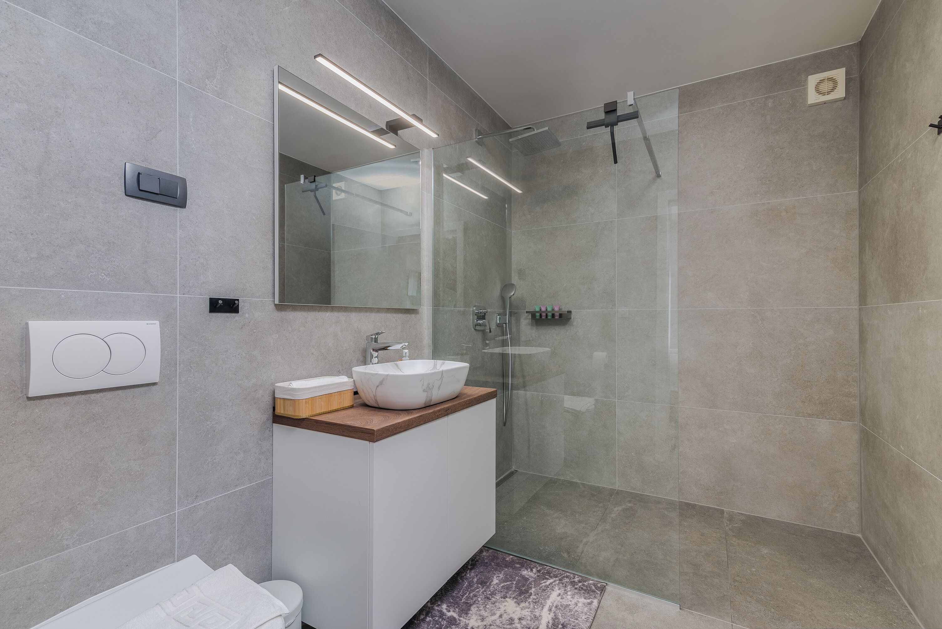 Een moderne badkamer met een douchecabine van glas, een wit wastafelmeubel met een marmeren blad en een grote spiegel.