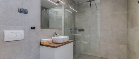 Een moderne badkamer met een douchecabine van glas, een wit wastafelmeubel met een marmeren blad en een grote spiegel.