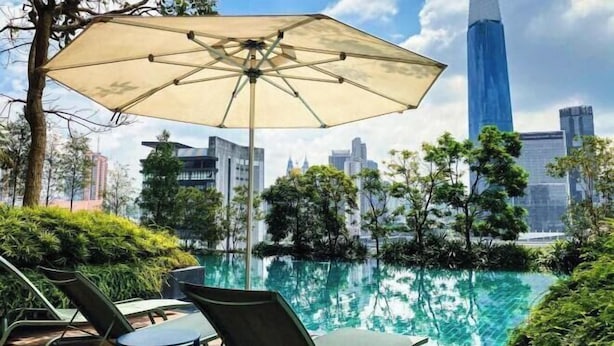 A poolside area with lounge chairs and an umbrella, overlooking a cityscape with modern buildings. - Continew Residence by Janice's Homestay (Kuala Lumpur)