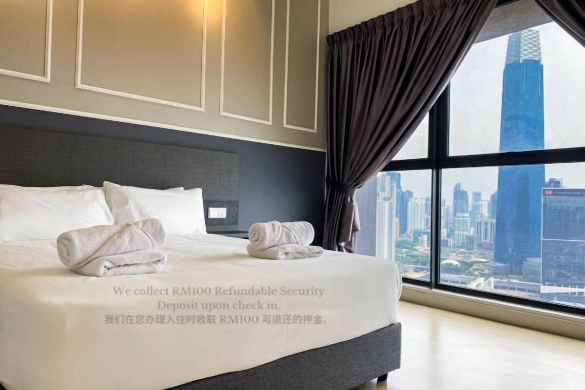 A hotel room with a large bed, a view of a cityscape, and a note about refundable security deposit.